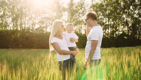 Junge-Eltern-Gehen-Mit-Weizenährchen-In-Weißen-T-Shirts-Und-Jeans-Aufs-Feld