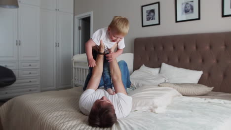 Dad-keeps-a-dignity-above-himself-lying-on-the-bed.-A-boy-in-a-white-T-shirt-laughs-and-smiles-from-playing-with-his-father