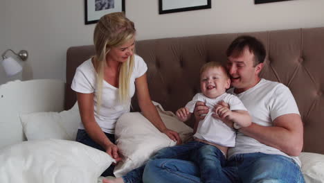 Loving-parents-play-with-their-son-on-the-bed-laughing-and-smiling-in-the-bedroom