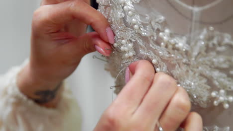 Close-up-fashion-designer-for-brides-in-his-Studio-pins-needles-lace-wedding-dress.-Seamstress-creates-an-exclusive-wedding-dress.-Secure-with-pins-and-needles-outline.-Small-private-business.-Sew-rhinestones-and-crystals-to-the-dress-thread-and-needle.-Jewelry-work.