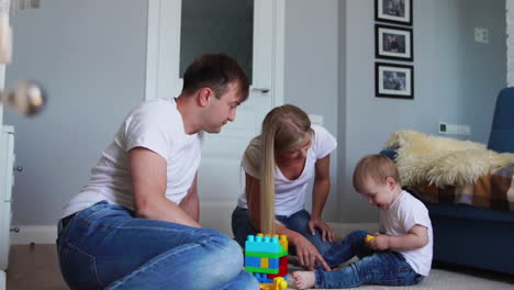 Happy-family-dad-mom-and-baby-2-years-playing-lego-in-their-bright-living-room.-Slow-motion-shooting-happy-family