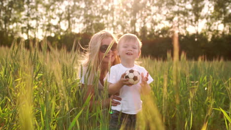 The-concept-of-a-happy-family.-In-the-rye-field-the-kid-walks-across-the-field-in-the-sun-setting-sun-looking-into-the-camera-Mom-stands-behind