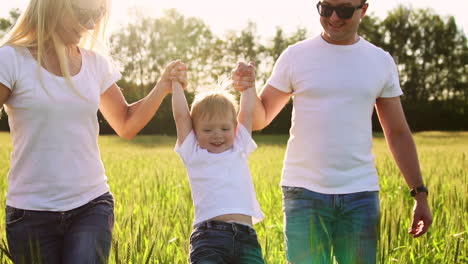 A-young-family-with-a-young-child-running-in-a-field-with-spikelets-of-wheat-swinging-a-boy-in-his-arms-who-laughs-and-smiles-with-happiness