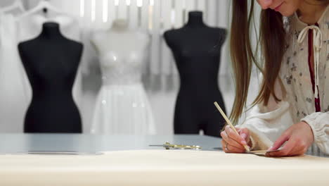 Schönes-Modedesigner-Mädchen,-Das-Auf-Papier-Mit-Goldenen-Scherenmustern-Für-Stoff-Auf-Schaufensterpuppen-Hintergrund-In-Hochzeitskleidern-Ausgeschnitten-Wurde.-Hersteller-Von-Brautkleidern.
