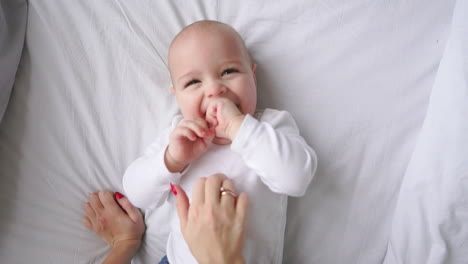 Baby-Im-Weißen-T-Shirt-Liegt-Auf-Einem-Weißen-Bett-Und-Lacht-Und-Blickt-In-Zeitlupe-In-Die-Draufsicht-Der-Kamera