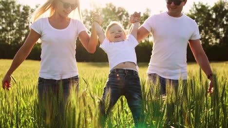 A-young-family-with-a-young-child-running-in-a-field-with-spikelets-of-wheat-swinging-a-boy-in-his-arms-who-laughs-and-smiles-with-happiness