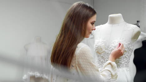 Portrait-of-a-girl-creating-a-wedding-dress-by-exclusive-order-sewing-fabrics-and-rhinestones-on-a-dress-dressed-in-a-mannequin.-production-of-wedding-dresses.-Little-business
