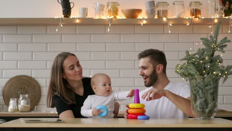 family,-holidays-and-people-concept---happy-mother,-father-and-little-daughter-playing-with-ring-pyramid-baby-toy-on-birthday-party