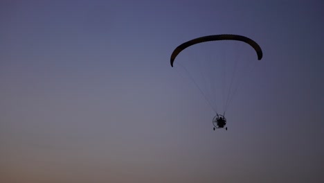 The-pilot-on-a-paraglider-flies-from-the-camera-gradually-moving-away-into-the-distance-against-the-sunset-beautiful-sky.-Beautiful-background-background-picture.-concept-of-freedom