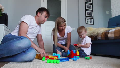 Happy-family-dad-mom-and-baby-2-years-playing-lego-in-their-bright-living-room.-Slow-motion-shooting-happy-family