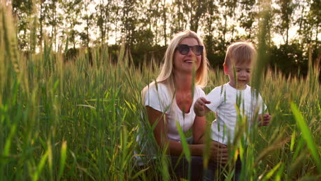 Loving-mom-and-son-hugging-and-playing-with-a-soccer-ball-in-a-field-with-spikelets-in-beautiful-sunset-light-in-white-t-shirts