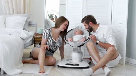 Close---up-of-happy-parents-watching-their-little-baby-sleep-in-a-rocking-chair-for-babies-at-home-in-a-white-apartment