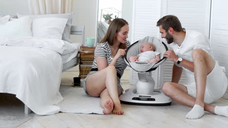 Close---up-of-happy-parents-watching-their-little-baby-sleep-in-a-rocking-infant-chair-at-home-in-a-white-apartment.-The-concept-of-minimalism