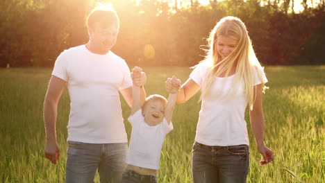 Mother-father-and-son-walk-in-the-field-with-spikes-in-white-t-shirts-and-jeans-fun-swinging-it-on-his-hands