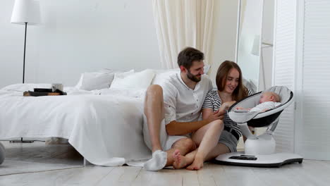 The-concept-of-a-modern-young-family.-Parents-watch-their-baby-sleep-in-a-special-device-for-sleeping-in-a-white-interior