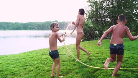 Sonniger-Sommertag-Auf-Dem-Rasen.-Familie-Mit-Zwei-Kindern-Hat-Spaß-Beim-Spielen-Mit-Wasser-Und-Beim-Lachen.-Fröhliche-Atmosphäre-Einer-Glücklichen-Familie