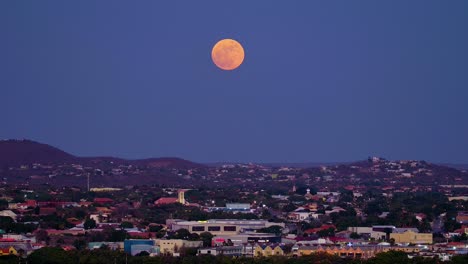 Schwenken-Sie-In-Der-Abenddämmerung-über-Die-Stadt-Willemstad-Auf-Curaçao,-Während-Der-Seltene-Blaue-Supermond-Rot-Vor-Dem-Violetten-Himmel-Aufgeht