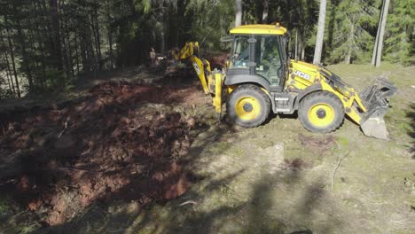 JCB-tractor-working-in-forest,-taking-out-tree-roots-and-throwing-them-into-pile