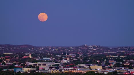 Pan-from-mountains-outside-willemstad-curacao-across-skyline-industrial-zone-to-full-supermoon,-red-against-purple-sky
