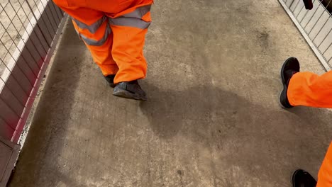 POV-Of-Group-Of-Feet-Walking-Wearing-Bright-Orange-High-Visibility-Trousers-At-Construction-Site