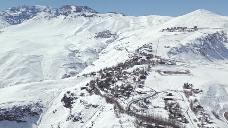 Luftaufnahme-Des-Verschneiten-Bergdorfes-Farellones-Mit-Dem-Exklusiven-Zentrum-Von-La-Parva-Und-El-Colorado-Im-Hintergrund-An-Einem-Sonnigen-Tag,-Chile