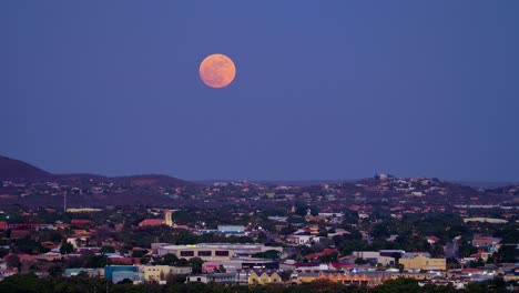 Large-full-blue-supermoon-glows-red,-pan-right-to-left-above-willemstad-curacao