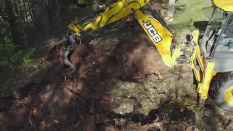 JCB-tractor-working-in-forest,-digging-out-tree-roots-from-sand-on-top-of-hill