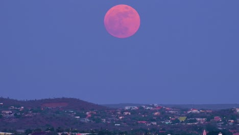 Pan-up-across-homes-on-hillside-of-willemstad-curacao-near-janwe-church-to-supermoon,-pink-and-red