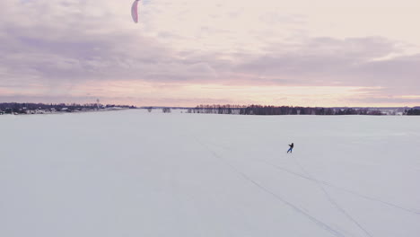 SLOW-MOTION:-A-male-athlete-is-engaged-in-kiting-on-skis.-He-rolls-on-the-ice-of-a-large-lake.-Rolling,-he-performs-various-jumps,-coups-and-other-exercises.-Windy-sunny-winter-day