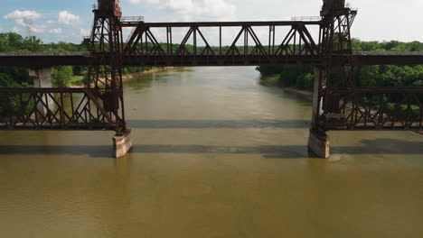 Rusty-truss-train-lift-bridge-over-White-River-near-Twin-City-Riverfront-Park,-De-Valls-Bluff,-Arkansas,-USA---Aerial-fly-under