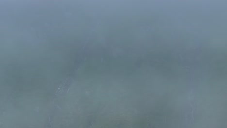Thick-fog-covers-meadow-below,-as-it-clears-waterfall-revealed