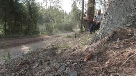 WRC-raly-spectators-film-on-their-phones-how-fast-rally-car-fly-s-bye-on-high-speed-on-gravel-road-surrounded-by-forest,-dust-cloud-is-seen-in-sunlight