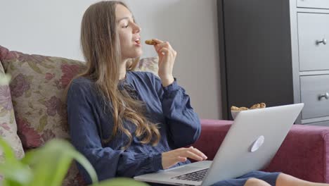 Woman-eating-cookies-while-using-laptop,-static-handheld