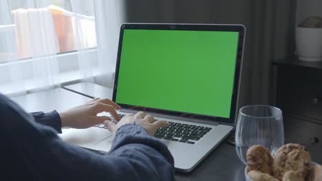 Woman-indoors-working-with-a-green-screen-laptop-on-the-table