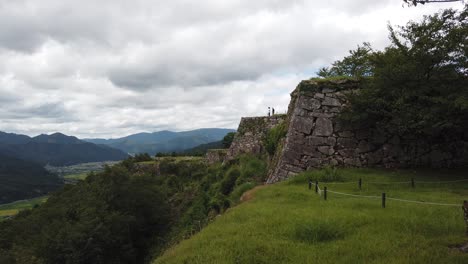 Lush-hilltop-of-Takeda-castle-overlooking-edge-of-mountain-valley,-ruins-of-ancient-Japanese-fortress