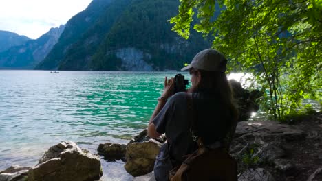 Tourist-woman-taking-a-photo-with-a-camera-in-the-shore-of-the-King's-Lake,-Königssee-in-Germany,-Bavaria