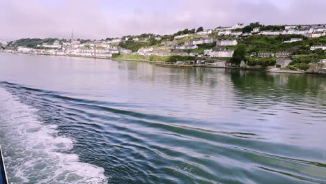 Approaching-Cobh-with-a-boat,-creating-wave-with-panorama-over-town,-a-town-in-Cork-county,-Ireland