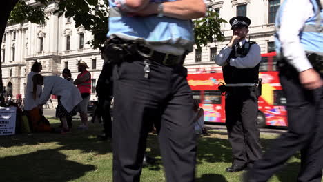 Four-Metropolitan-police-officers-stand-in-the-shade-under-a-tree-and-two-officers-walk-off-as-they-all-monitor-a-gathering-protest-on-Parliament-Square-during-a-heat-wave