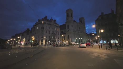 Nightlife-at-the-streets-of-Besançon-in-France,-with-cars,-tram-tracks,-people-walking,-night-sky-and-streetlights