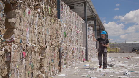 Worker-counts-bales-of-cardboard-and-paper-at-recycling-plant,-slomo
