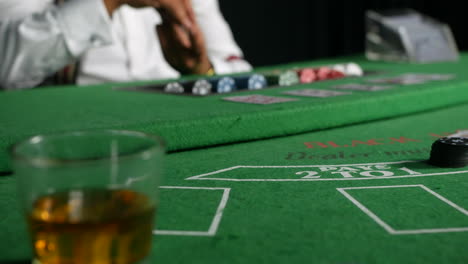 A-poker-dealer-croupier-paying-out-chips-close-up-next-to-a-glass-of-whiskey-on-a-black-jack-table-in-a-casino-to-the-winning-player