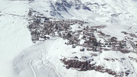 Establishing-aerial-view-above-Farellones-winter-mountain-pine-forest-and-snow-covered-neighbourhood-houses