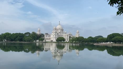 Shot-of-white-marble-monument-called-Victoria-Memorial-compound-with-a-lake-in-foreground-in-Kolkata,-West-Bengal,-India-on-a-cloudy-day