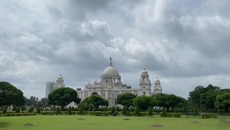 Tilt-up-shot-of-beautiful-historic-white-marble-monument-called-Victoria-Memorial-with-white-clouds-passing-by-in-the-background-in-Kolkata,-India-on-a-cloudy-day