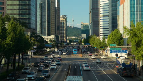 Sinyongsan-Bahnhof-In-Der-Innenstadt-Von-Seoul,-Reger-Verkehr-Auf-Der-Hangang-Daero-Straße-Mit-Hohen-Bürogebäuden-Rundherum-Und-Blick-Auf-Den-N-Namsan-Turm-–-Erhöhte-Ansicht-Bei-Tag-–-Herauszoomen