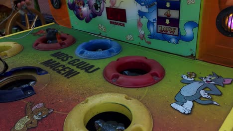 Kid-playing-with-Whac-A-Mole-arcade-game-in-park,-hitting-quickly-with-sponge-hummer-hamsters-appearing-on-holes