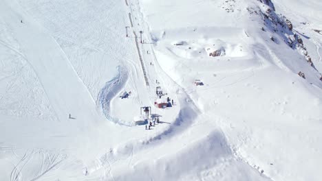 Aerial-view-looking-down-over-winter-tourists-starting-to-ascend-ski-resort-lift-on-steep-snow-covered-mountain-slope