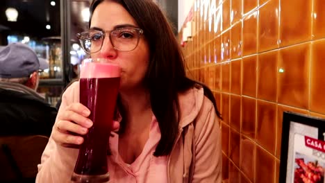 Slow-motion-footage-of-woman-savoring-red-beer-in-lively-bar-at-night