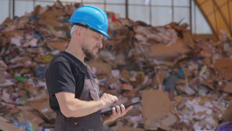 Worker-at-outdoor-recycling-plant-uses-tablet,-half-body-side-shot
