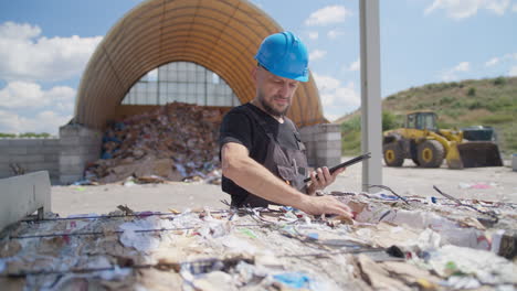Male-worker-with-tablet-checks-paper-bale-at-outdoor-recycling-plant